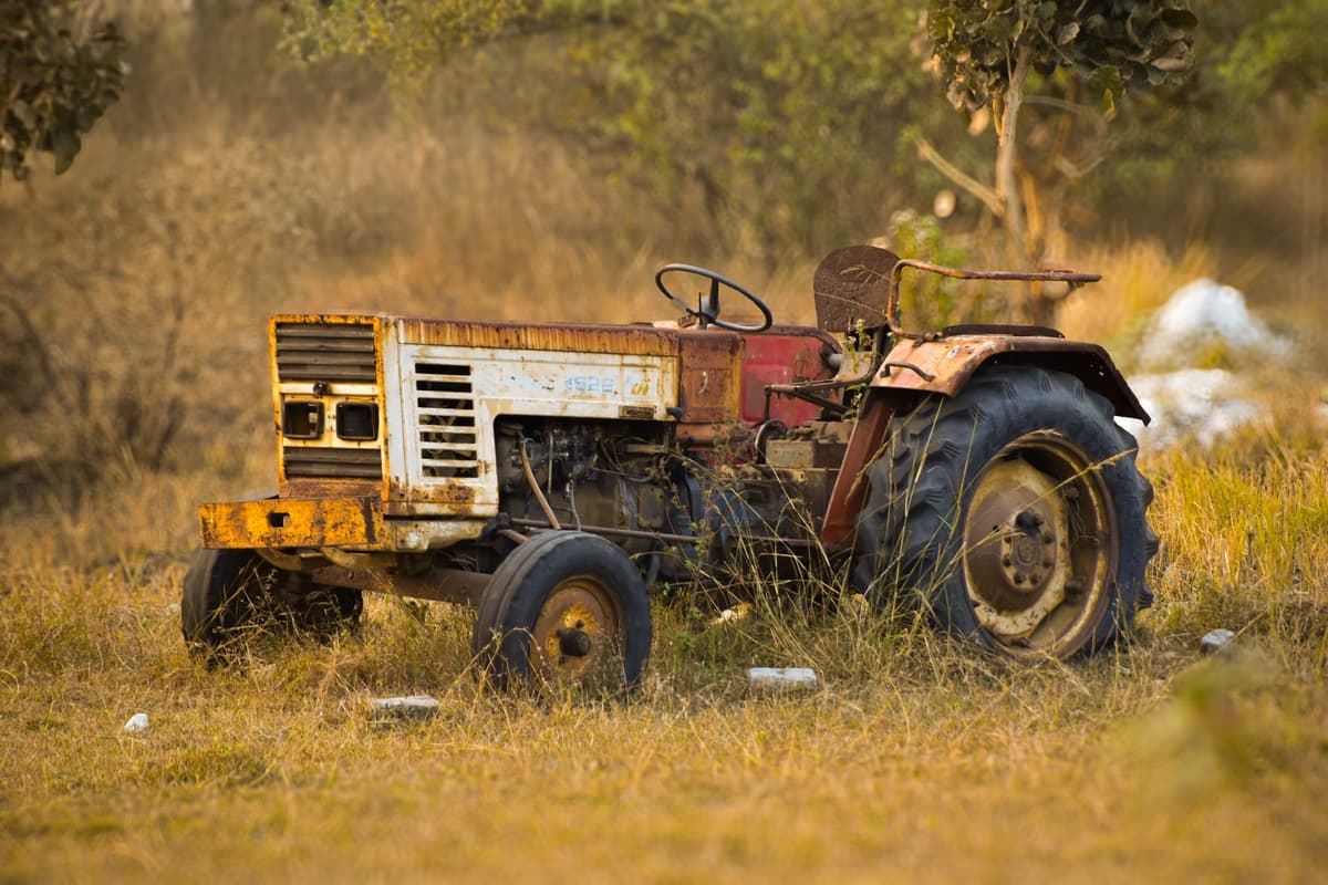 a rusted tractor abandoned in a field of tall weeds