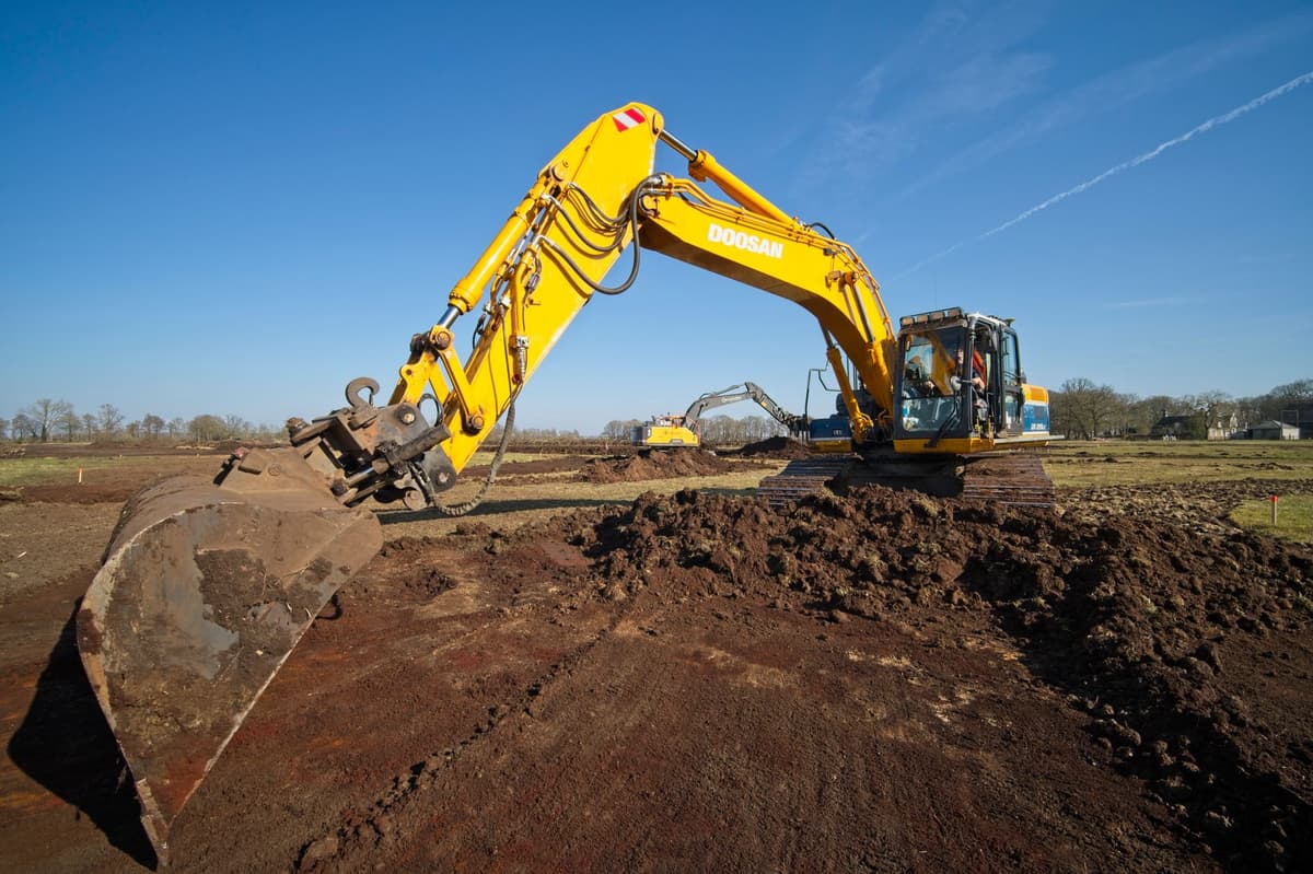 a single yellow excavator in a vast flat dirt field