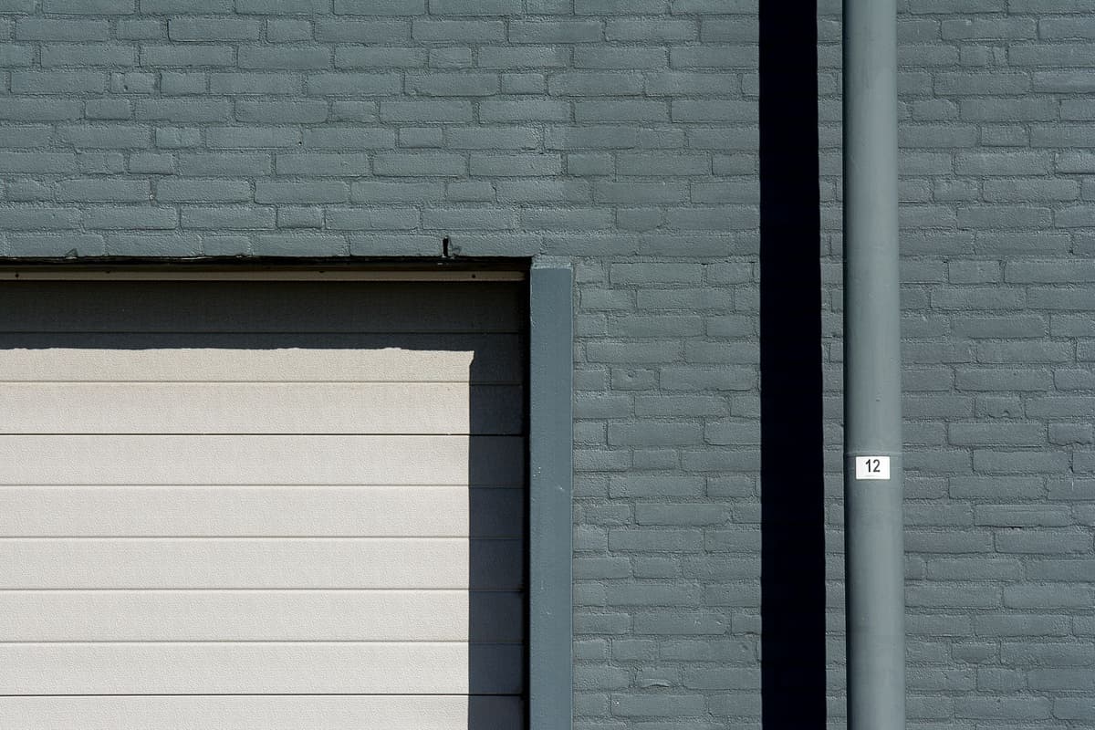 a large insulated pipe connecting a gray industrial building to a modern apartment complex