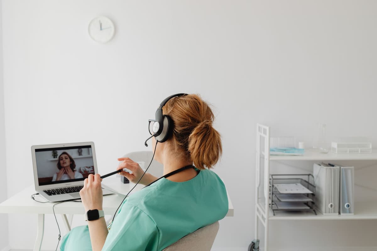 a doctor staring at a laptop screen while a patient talks to their back