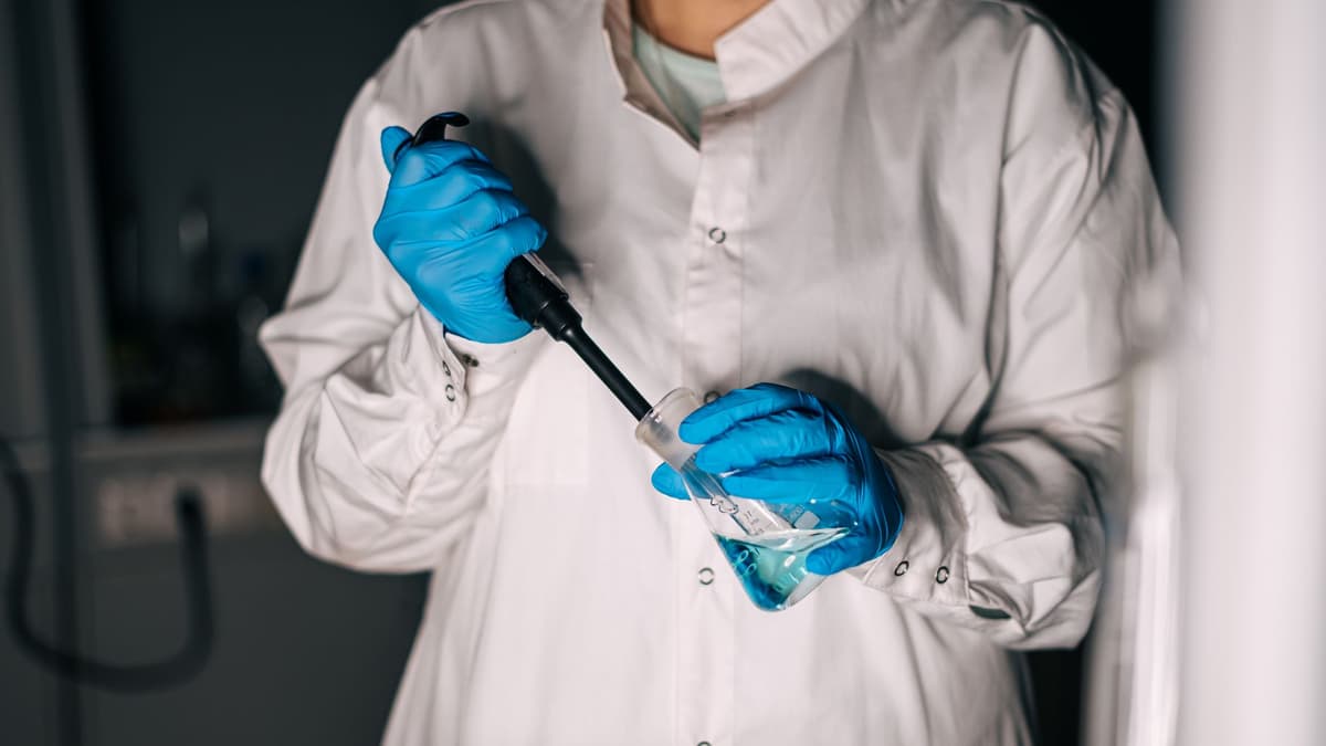 a scientist in a lab coat staring at a glowing steel vat holding a single spear