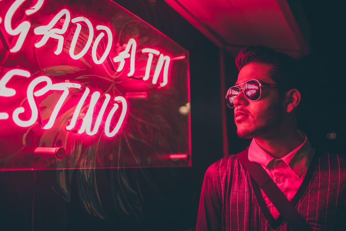 a man wearing 80s neon sunglasses looking at a night sky filled with glowing logos
