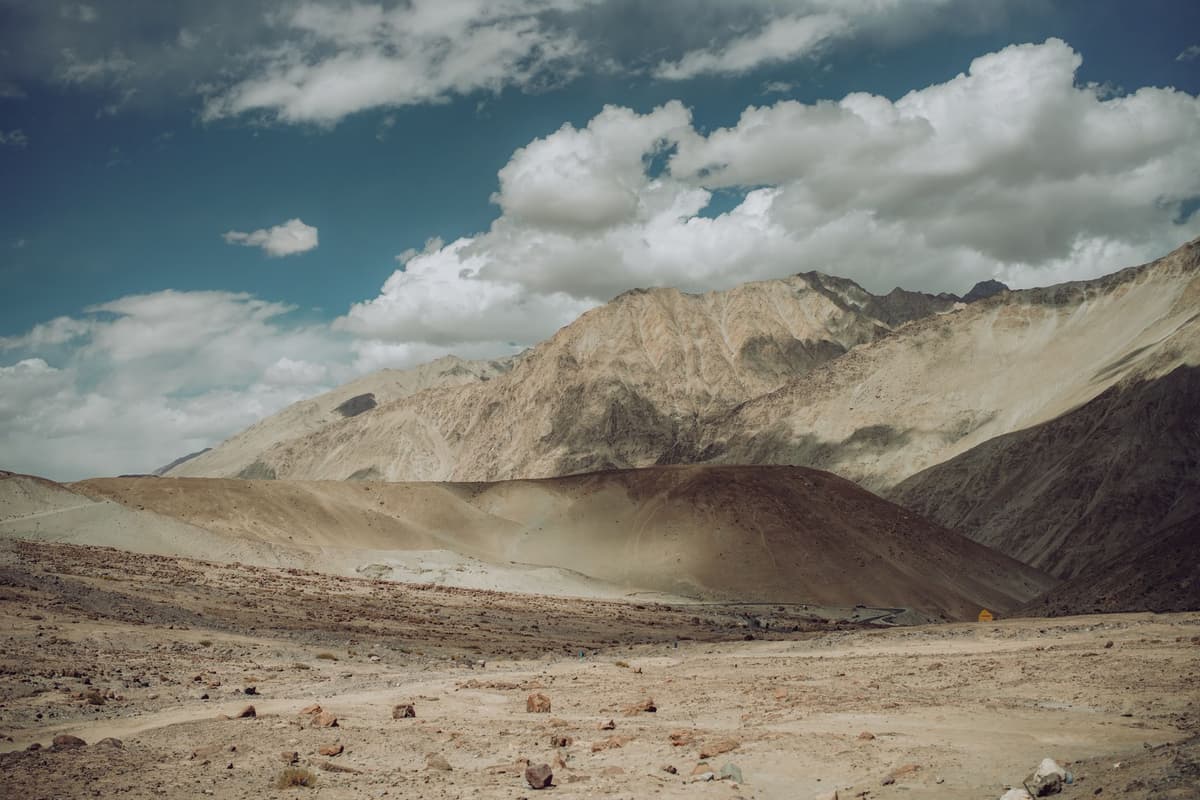 A dry, dusty mountain valley under a stark blue sky with a shrinking white glacier in the far distance