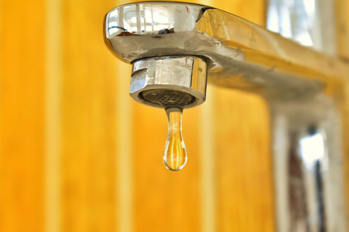a stainless steel laboratory faucet dripping into a glass beaker