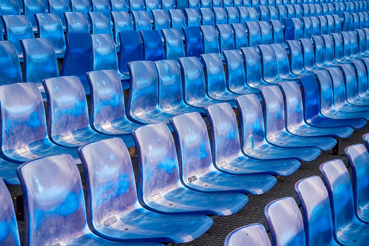 a row of empty blue stadium seats under grey skies