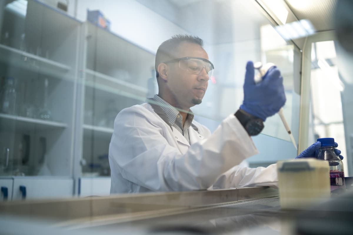 a scientist in a lab coat using a pipette on a single ramen noodle